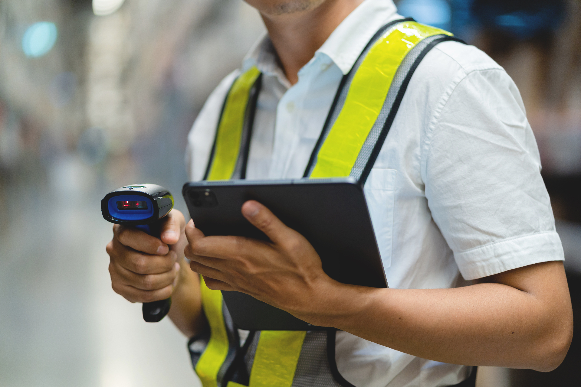 Warehouse worker in a hi-vis vest using a handheld scanner alongside a tablet