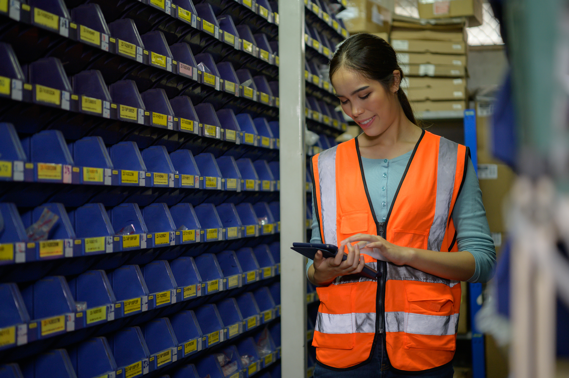 Warehouse worker in a high-visibility vest using a tablet next to parts shelving